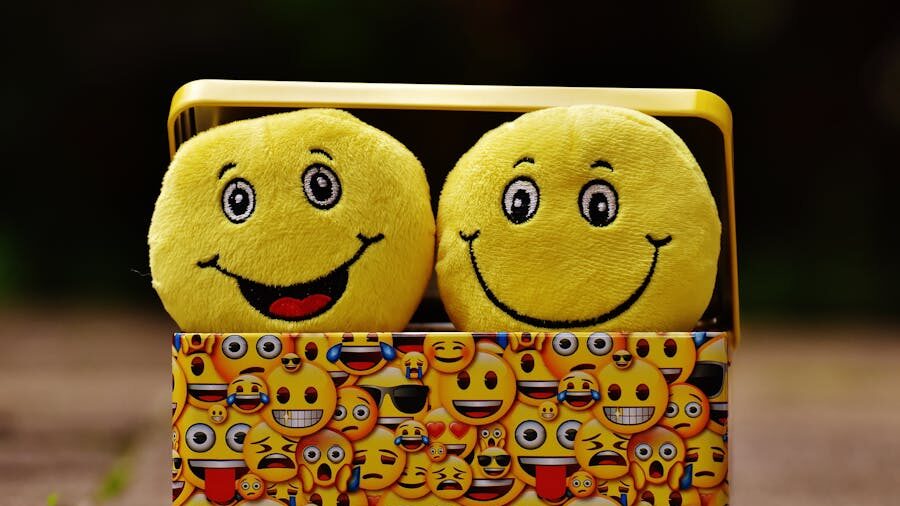 Two smiling yellow emoji plush toys in a decorative box covered with various emoji faces, symbolizing humor and connection.
