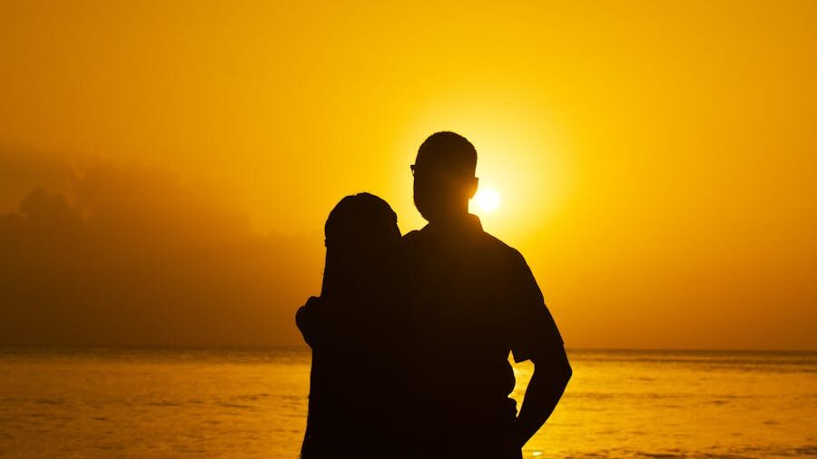 Silhouette of a couple embracing at sunset by the ocean, surrounded by golden light and calm waters.