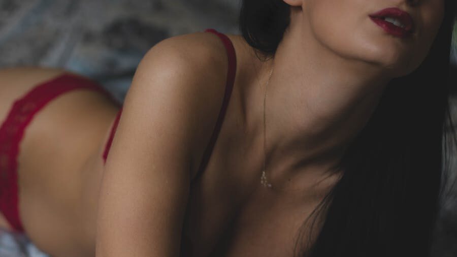 A close-up of a woman in red lingerie lying down, partially out of frame, with focus on her lips, neckline, and jewelry, evoking sensuality and challenging superficial judgments.