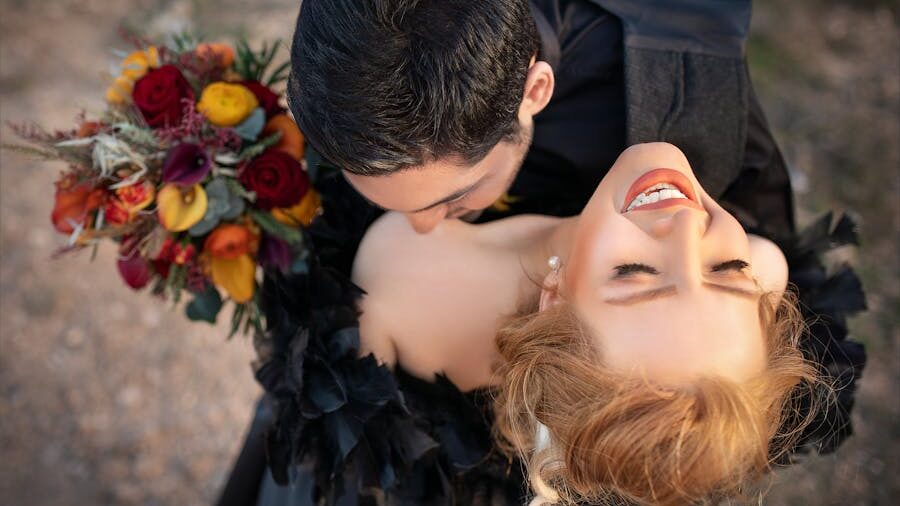 A joyful couple embraces closely, with one partner holding a vibrant bouquet and the other smiling blissfully, capturing a moment of deep emotional connection.