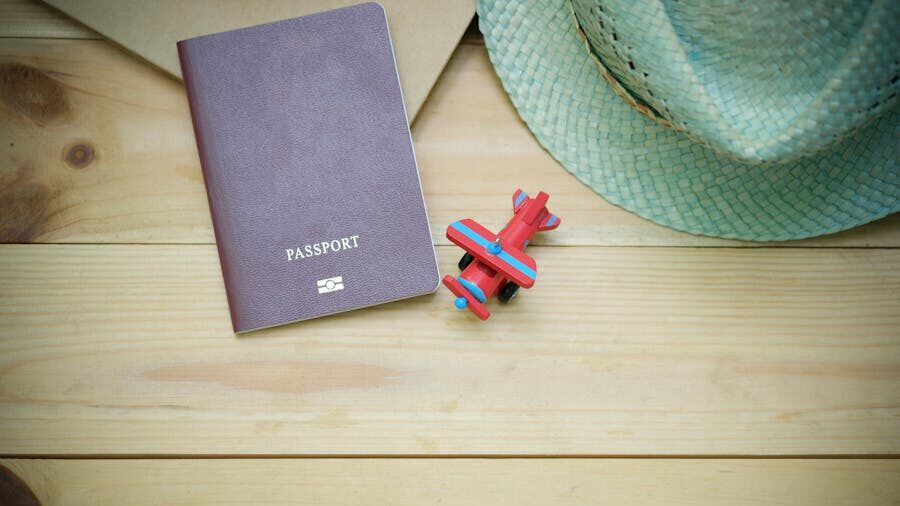 A passport, a straw hat, and a toy airplane on a wooden surface suggest plans for upcoming travel.