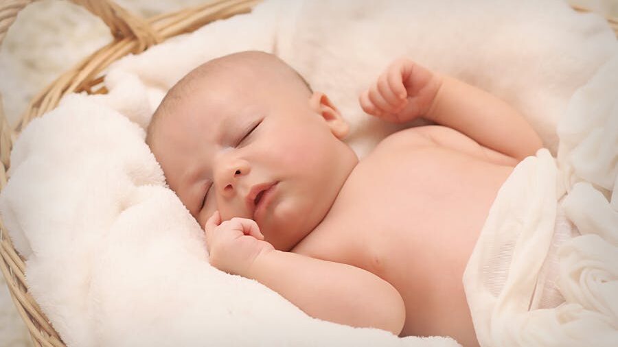 Sleeping baby with bare skin wrapped in white fabric, captured in a serene pose within a natural woven basket.