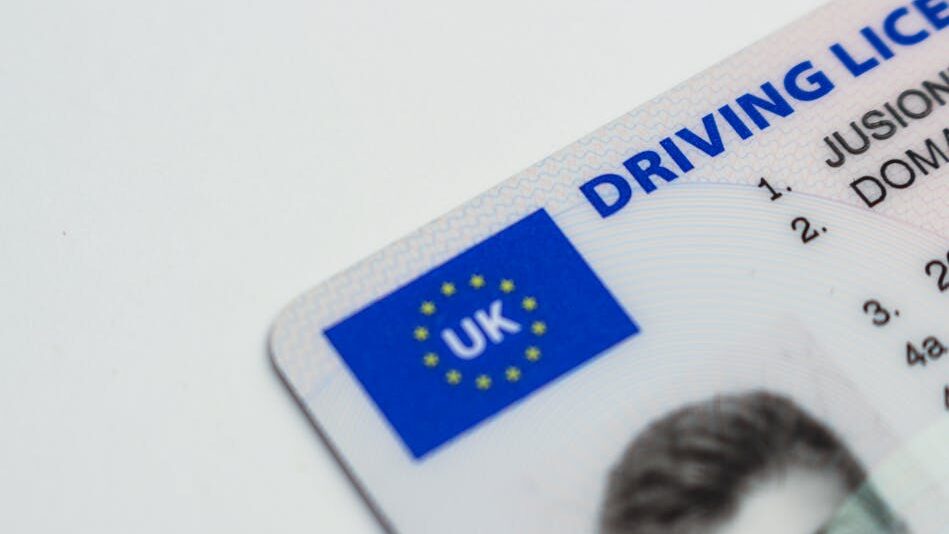 UK-issued driver’s licence with official markings, name text, and part of a portrait on a white surface.