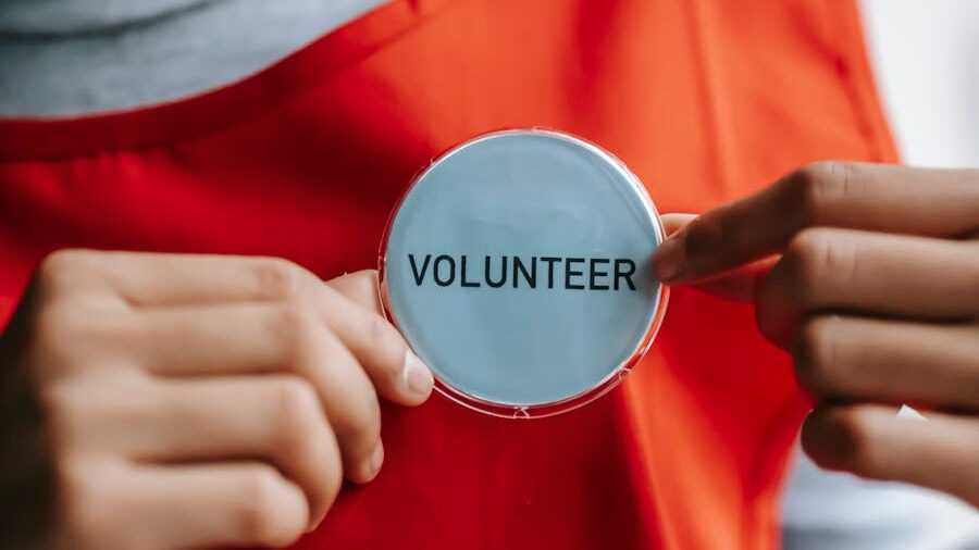 Hands holding a circular volunteer badge, representing community support and personal commitment.