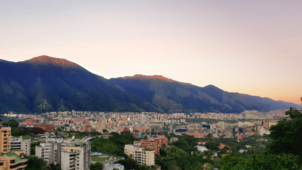 View of Caracas with dense buildings in front of Ávila mountain under a soft evening sky.