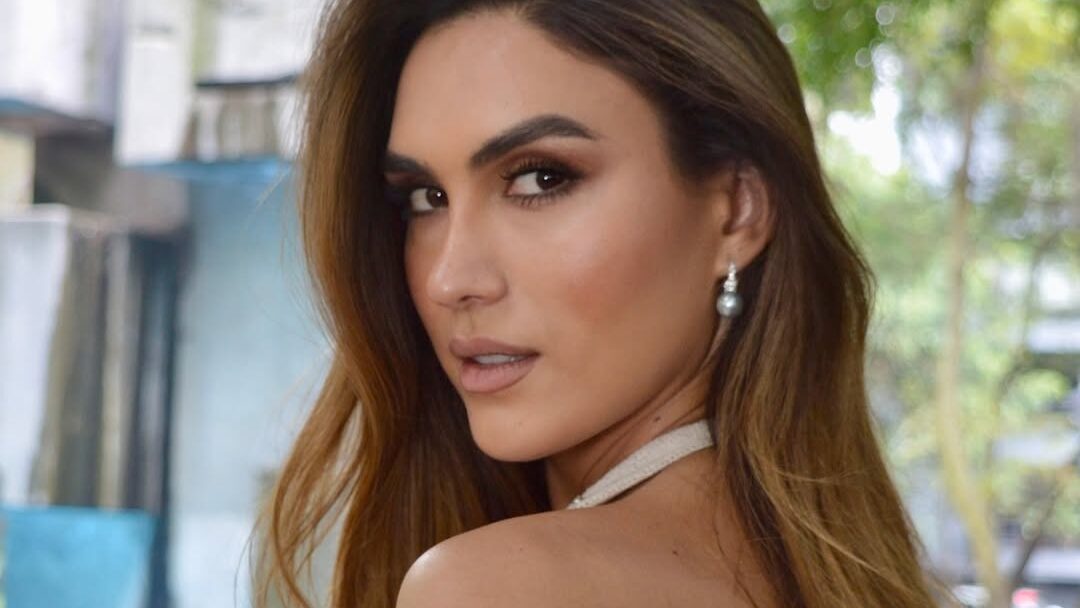 Isabella Santiago turns toward the camera in a white halter dress outdoors.