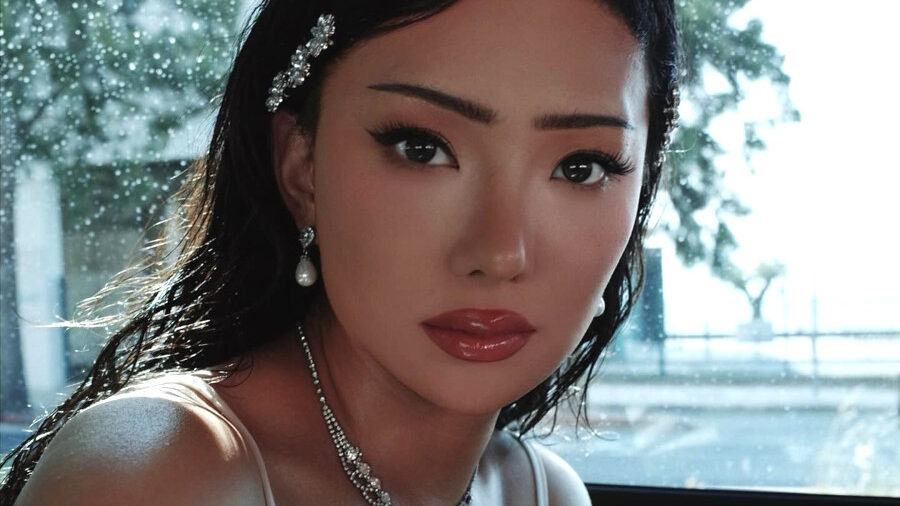 Nikita Dragun seated in a car in Lisbon, wearing a white lace outfit and pearl jewelry.