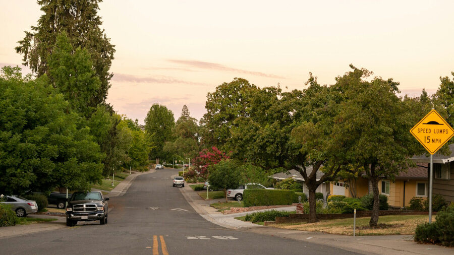 View of a Sacramento neighborhood street lined with trees and homes, captured during evening light.