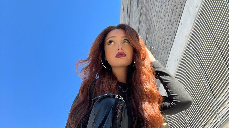 Zoey Luna photographed in May 2024, crouched in front of a building, wearing leather pants and long curled red hair.