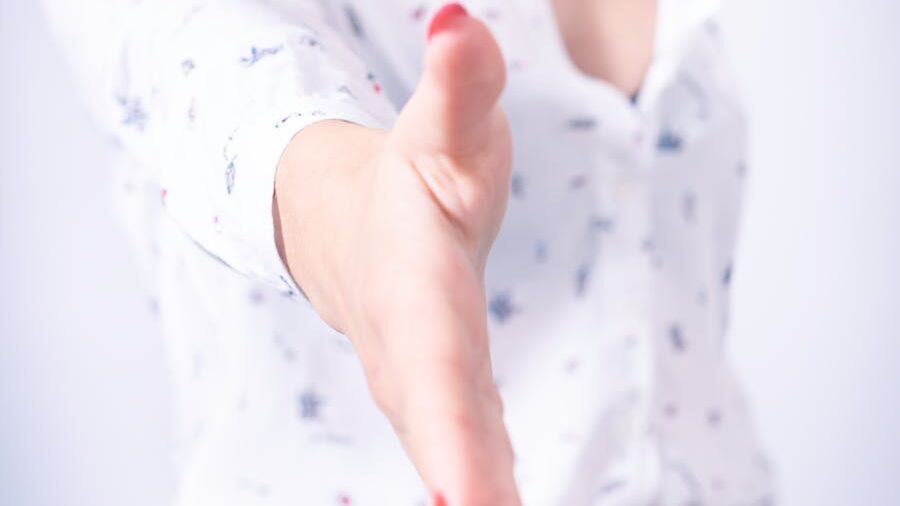 A woman in a white shirt reaching out with her hand, offering a handshake as a sign of welcome or agreement.
