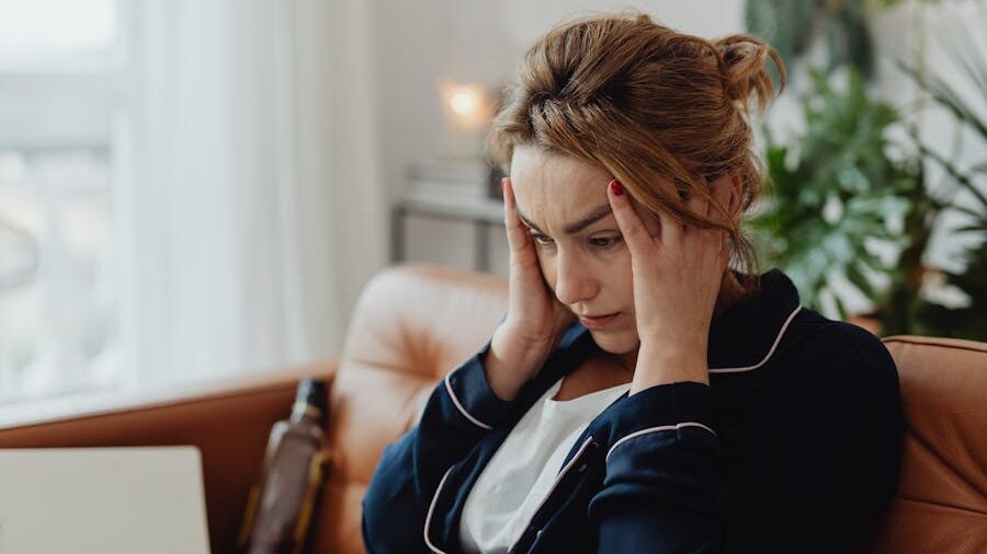 Woman with her hands on her temples sitting on a couch, looking down in a stressed or worried emotional state.