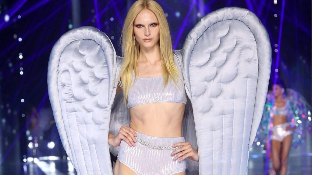 Alex Consani poses in shimmering silver two-piece set with angel wings at Victoria’s Secret 2024 fashion show.