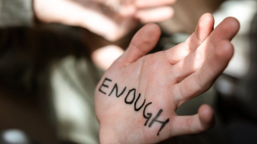 Close-up of an open hand with the word “ENOUGH” written in black marker across the palm.