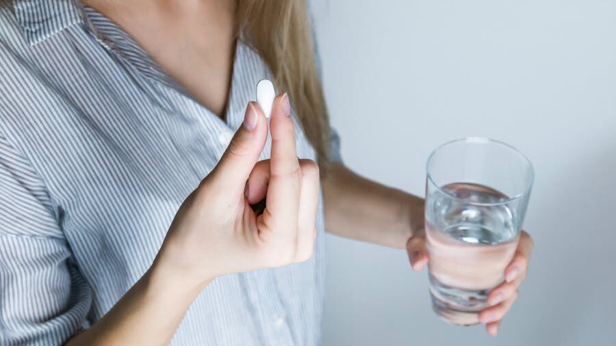 Close-up of an individual preparing to take a pill, holding medication and a glass of water.