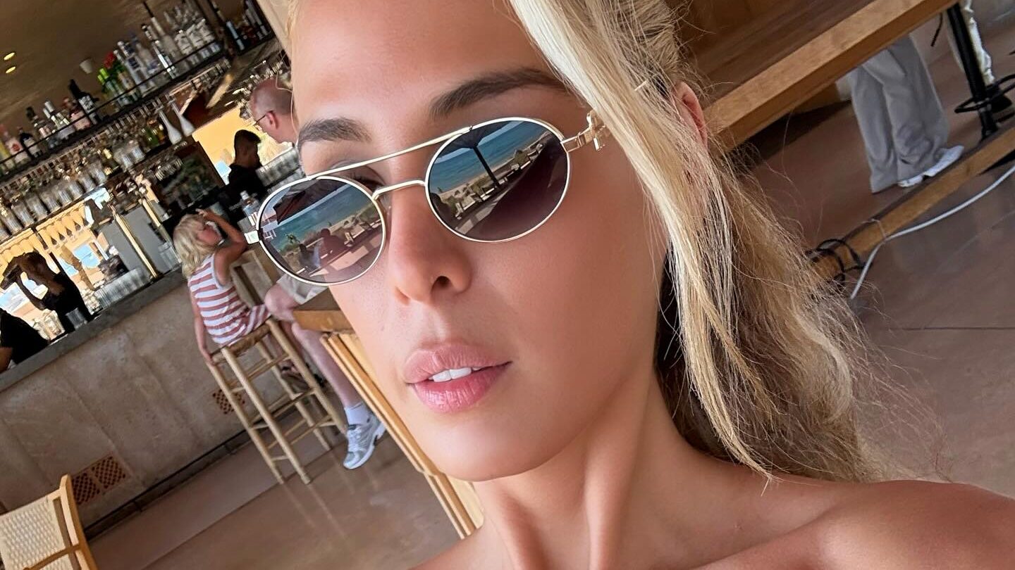 Carmen Carrera taking a selfie indoors in Palma de Majorque, wearing sunglasses and a strapless top in a bar setting.