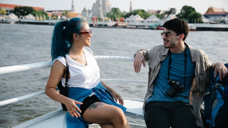 Smiling couple sitting on a riverboat, city landmarks and water in the background.