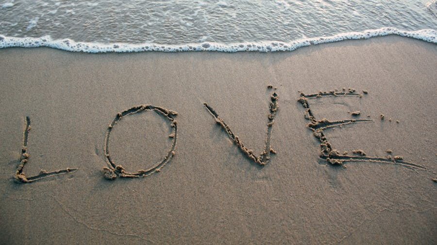 Letters forming the word “love” drawn in sand on a beach, with water from the sea slowly reaching them.