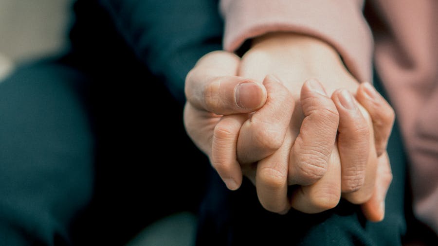 Detail of two people holding hands closely, conveying comfort, trust, and emotional support.