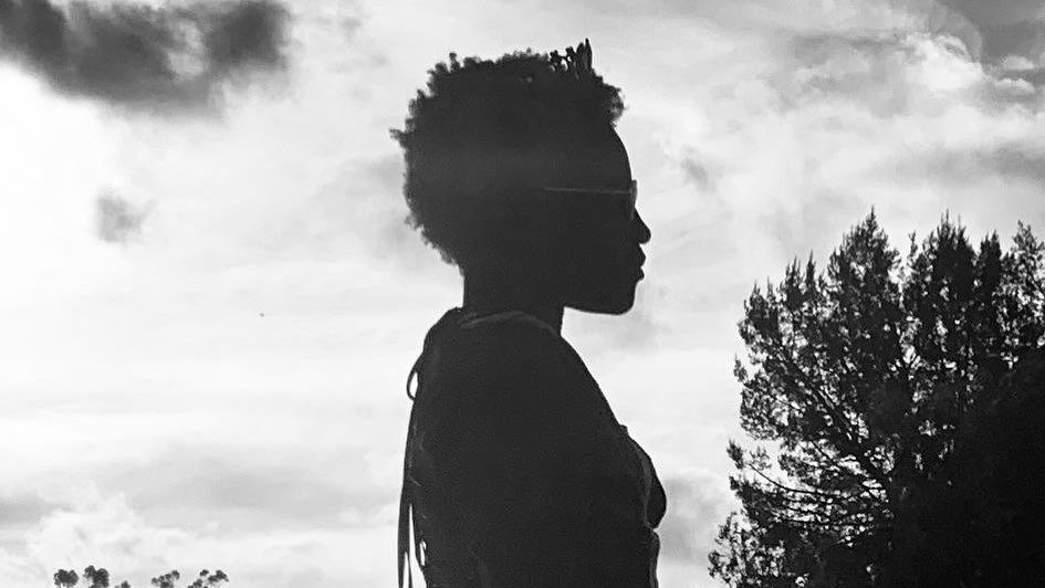 Black-and-white photo of Zaya Wade standing outdoors in profile, with trees and sky in the background.