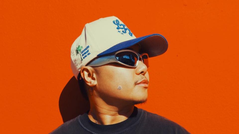 Jake Zyrus wearing sunglasses and a cap, posing in front of a vivid orange wall, shadow casting behind him.