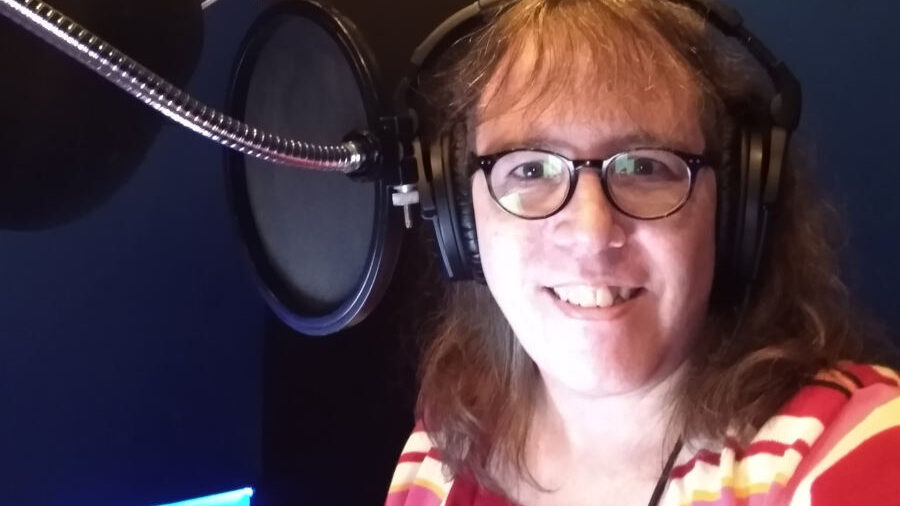 Julia Serano in a recording studio wearing headphones, smiling beside a microphone after finishing her audiobook recording.