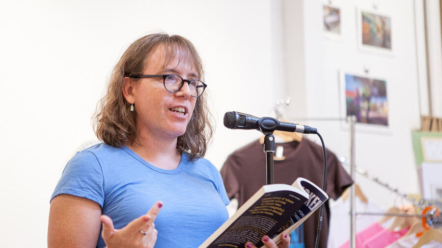 Julia Serano reading from her book Outspoken at a podium in 2017, speaking into a microphone while holding a copy.