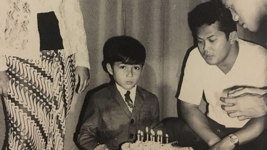 Vintage black-and-white photograph of Dena Rachman as a child standing with family members during a birthday celebration.