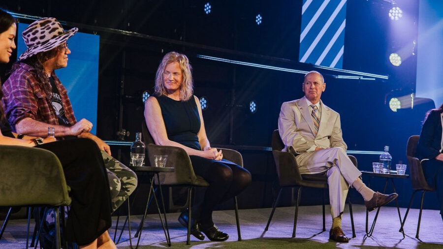 Vivienne Ming sits on a panel discussion stage at The Next Web in Amsterdam alongside other speakers under blue lighting.