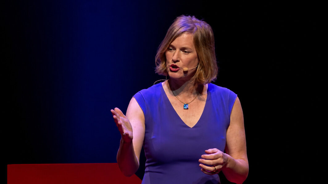 Vivienne Ming speaks on stage during her TEDxBerkeley presentation, wearing a blue dress and a headset microphone.