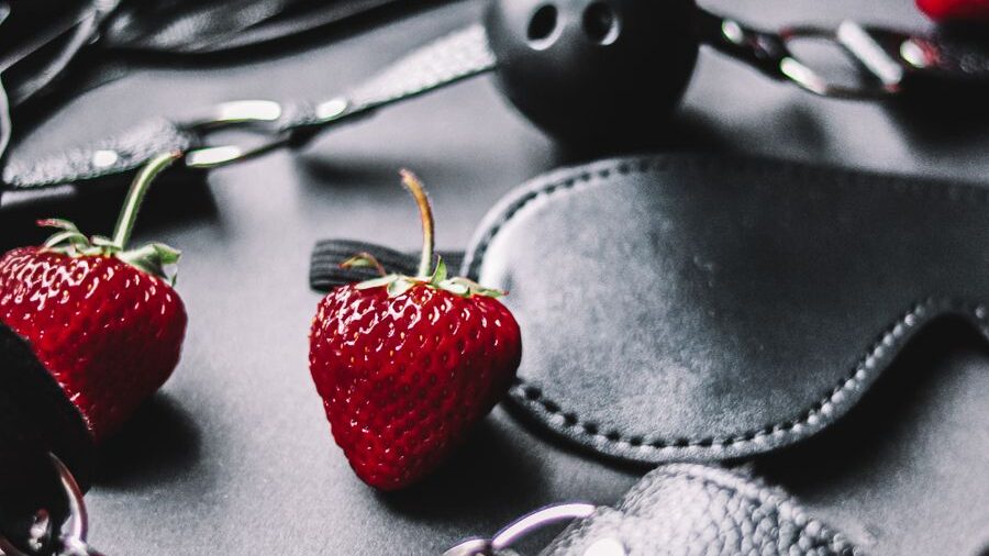 Red strawberries contrasted against dark leather accessories, with textured materials and metallic details visible.