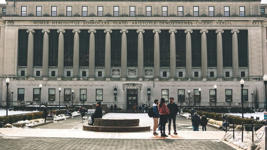 Front view of Columbia University Library in New York City, featuring large columns, an open plaza, and visitors outside.