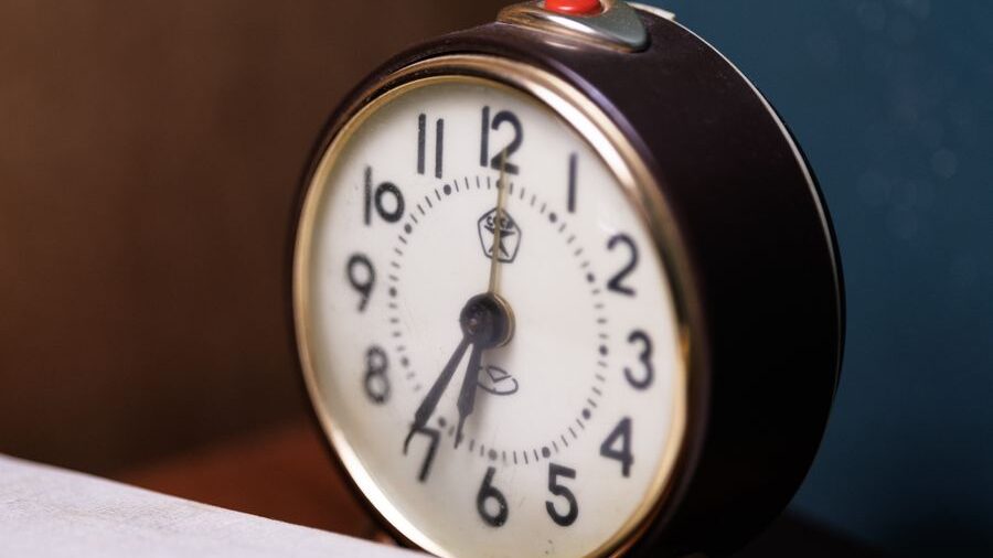 Black bedside alarm clock displaying the time, photographed up close with a blurred indoor background.