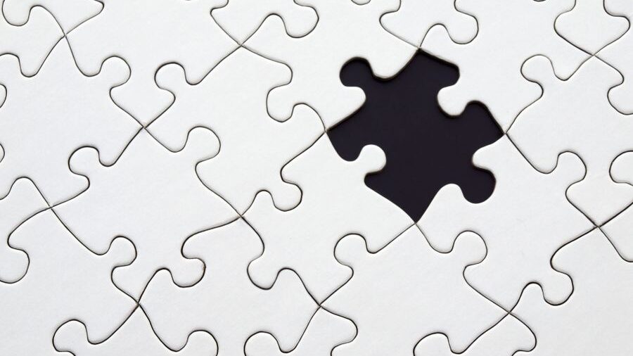 Interlocking white puzzle pieces viewed from above, with one central section missing from the arrangement.