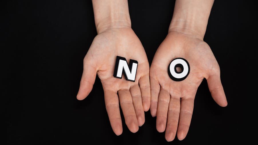 Two open hands against a black background holding the letters N and O, forming the word “NO” in white blocks.
