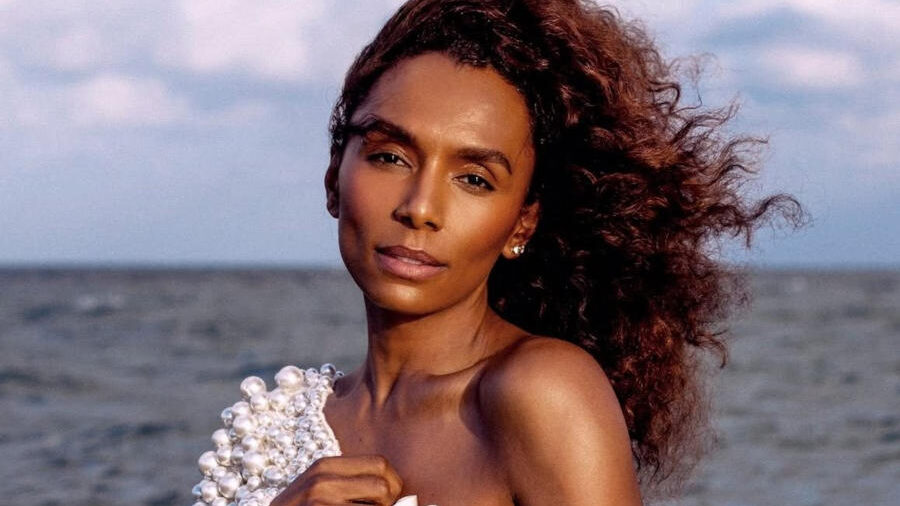 Editorial portrait of Janet Mock by Lia Clay for Out Magazine. She wears a white pearl-covered couture outfit during a seaside photoshoot.