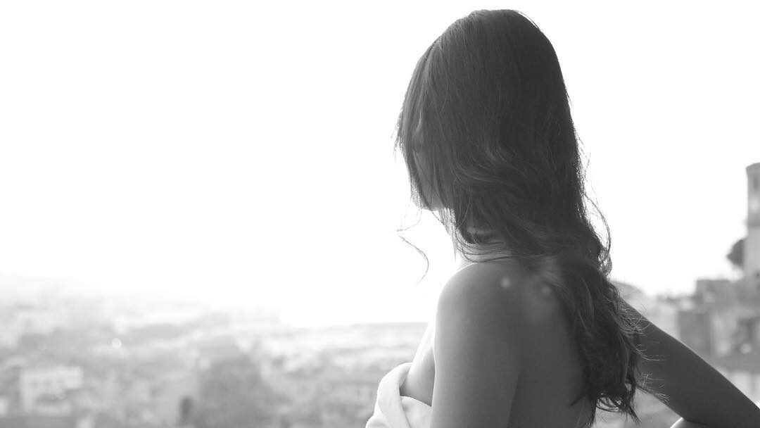 Black-and-white photo of Zion Moreno standing on a balcony, wrapped in a towel and gazing over a sunlit city skyline.