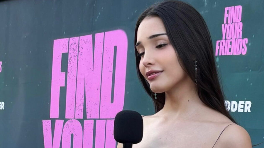 Zion Moreno wears a sleek black dress while holding a microphone on the red carpet at the Find Your Friends premiere event.