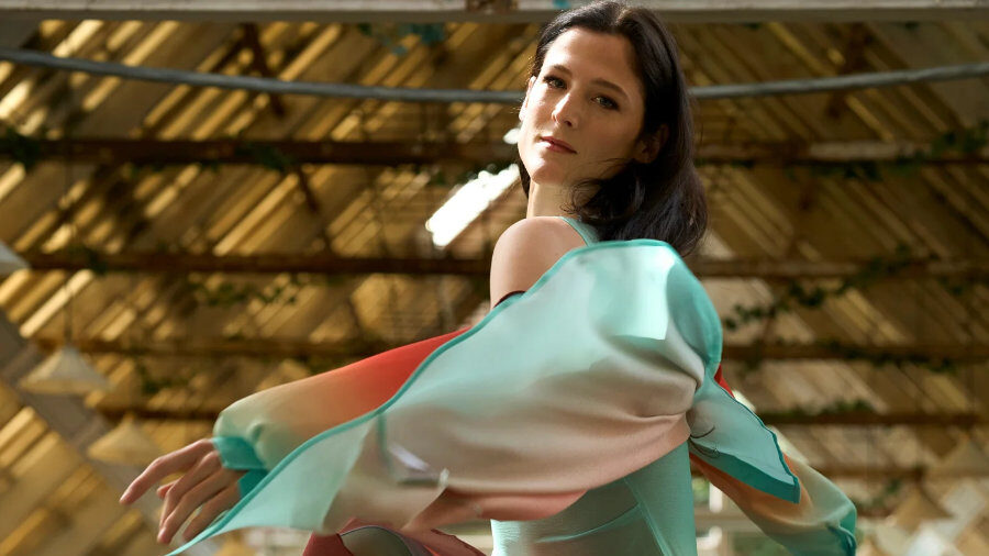 Nora Monsecour captured in motion wearing a colorful flowing outfit inside a bright industrial-style space.