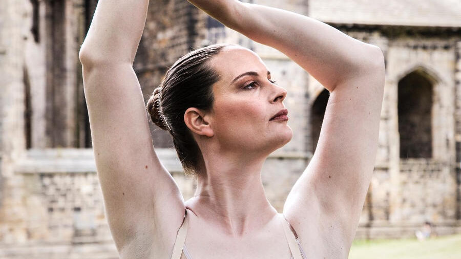 British ballet dancer Sophie Rebecca posing with her arms raised in a pink and blue ballet costume for World Ballet Day 2022.