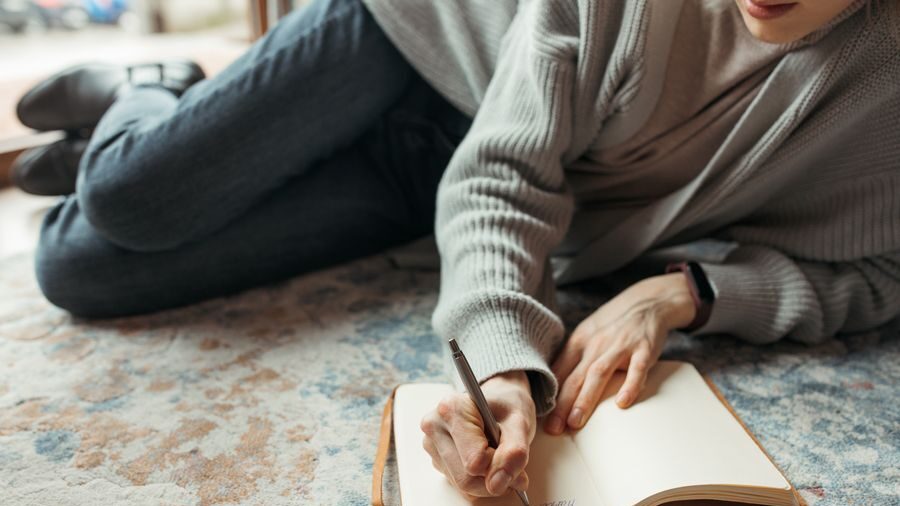 A person lying on a rug and writing in an open notebook while reflecting on their past dating experiences.
