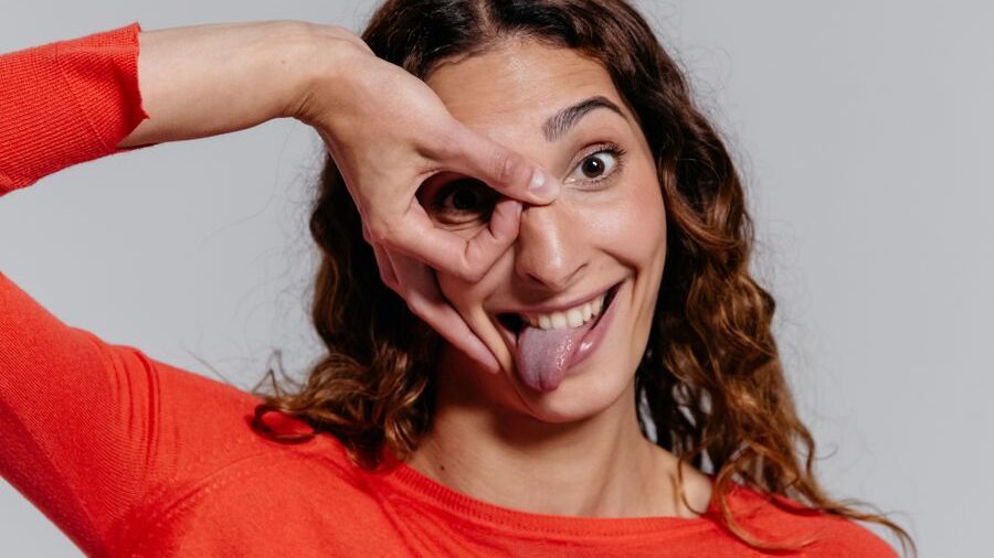Woman in a red top smiling, sticking out her tongue and making a circle around one eye with her fingers