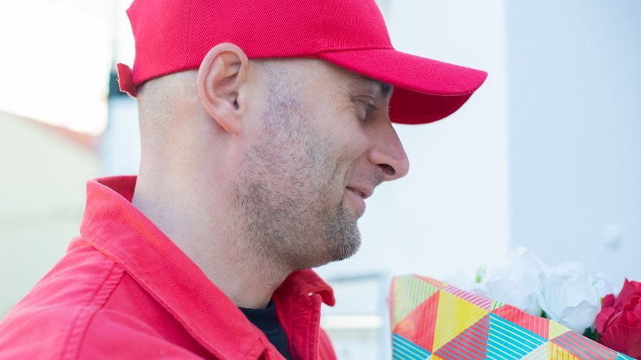 Side profile of a man wearing a red baseball cap and matching shirt, looking at a colorful gift bag with flowers.