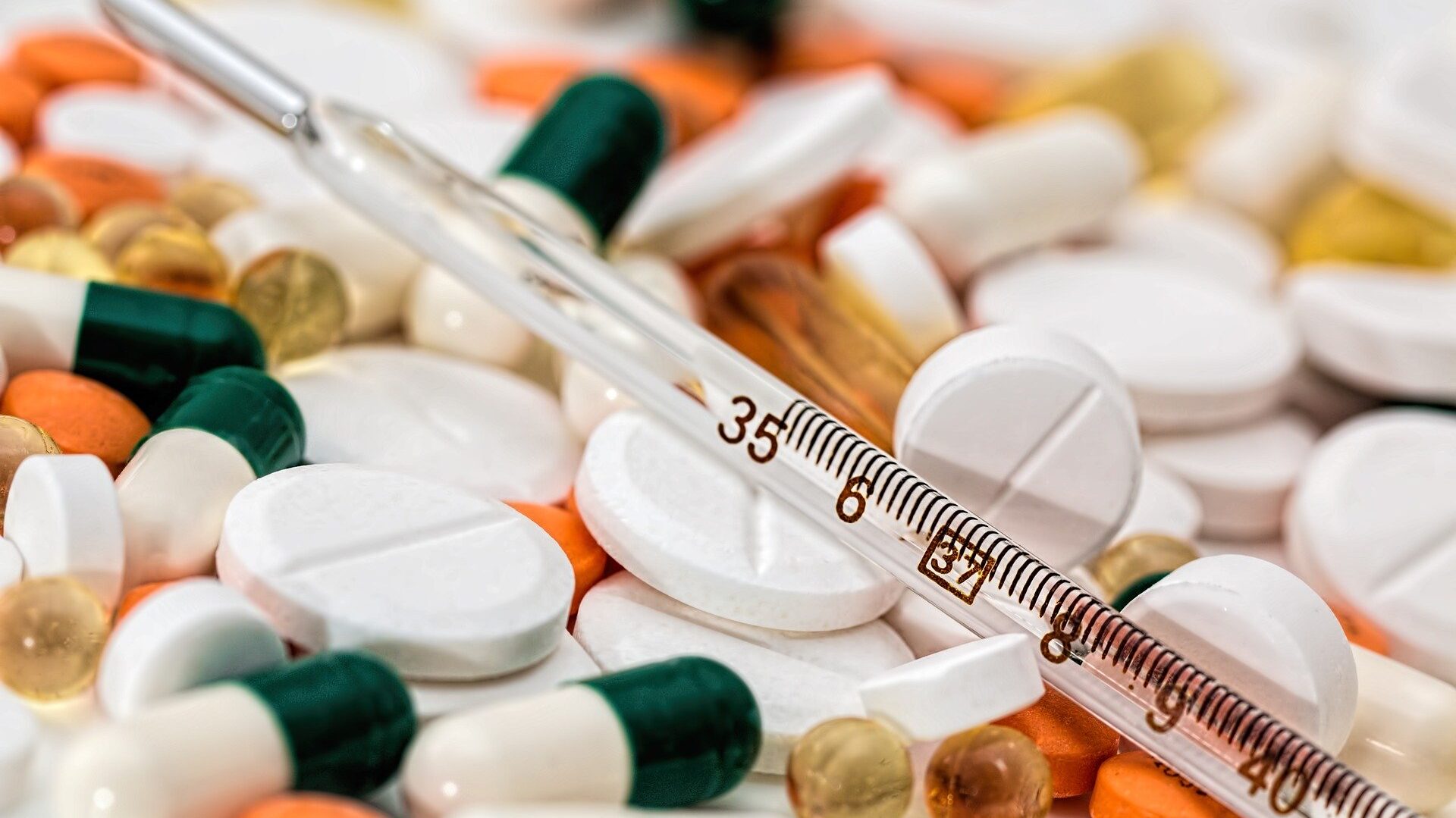 Primer plano de píldoras variadas y un termómetro que simbolizan el tratamiento médico.