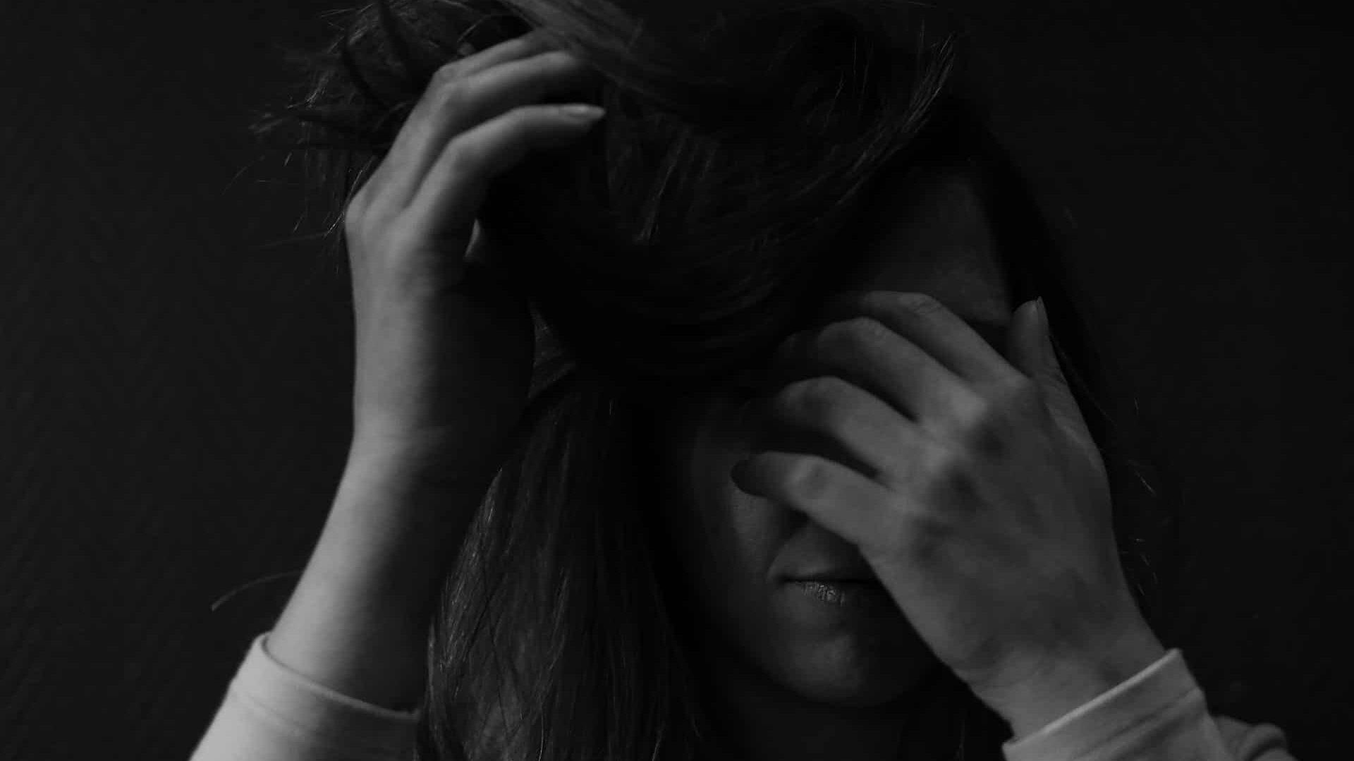 Primer plano en blanco y negro de una persona cubriéndose la cara con las manos que transmite angustia o agobio emocional.