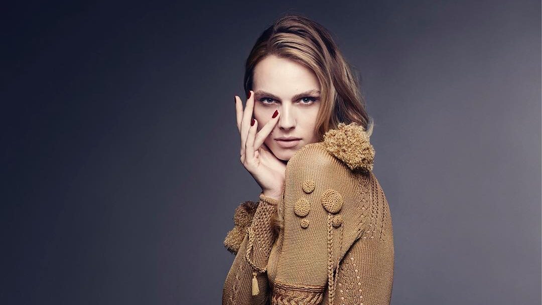 Andreja Pejić con un vestido escultural, dorado y con textura de Giles Deacon mientras posa con gracia en un retrato editorial de estudio.