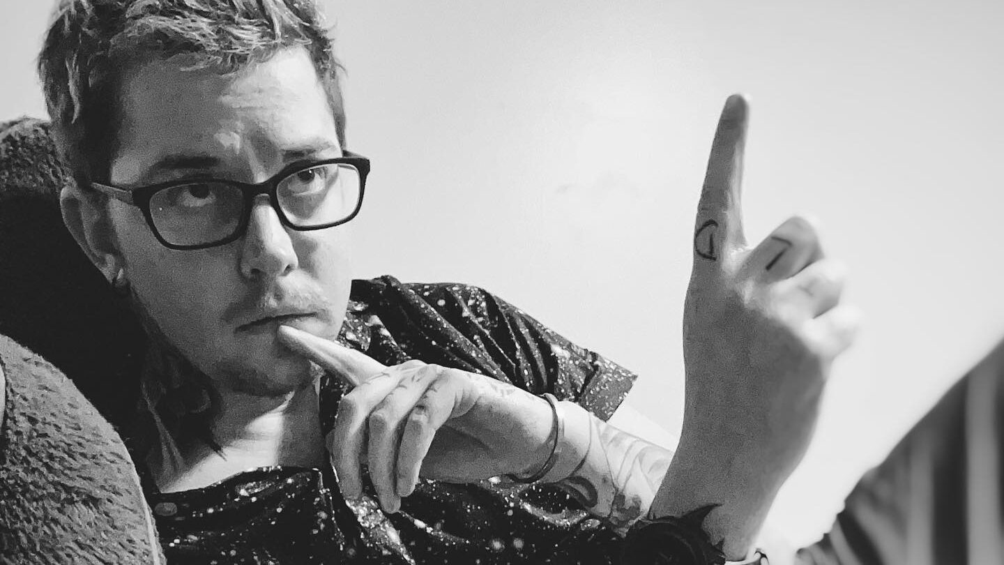 Foto en blanco y negro de Skylar Kergil recostado en una cama, pensativo, con un dedo en los labios y apuntando hacia arriba.