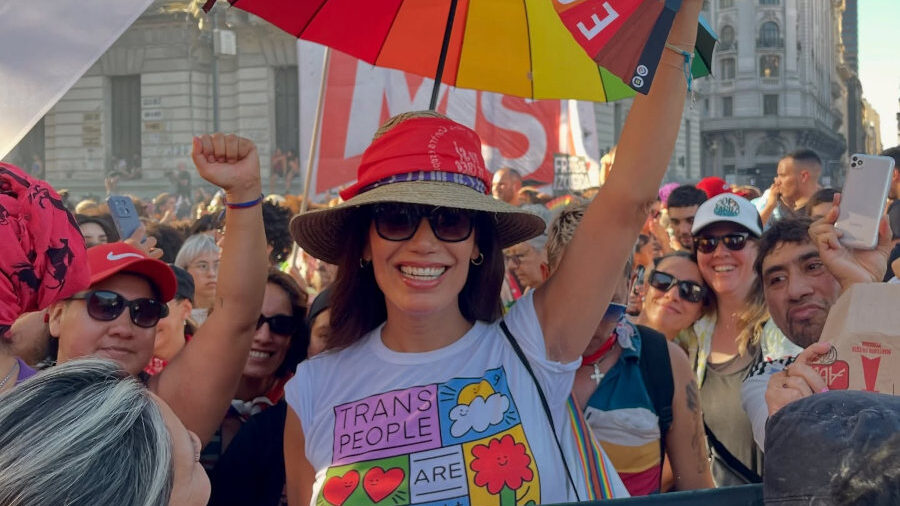 Florencia De La V sonriente en Plaza de Mayo, rodeada de manifestantes y banderas del arcoíris.