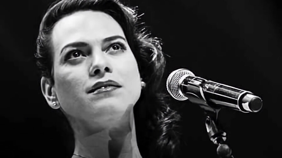 Foto en blanco y negro de Daniela Vega frente a un micrófono en el escenario, mirando hacia arriba con una iluminación suave.