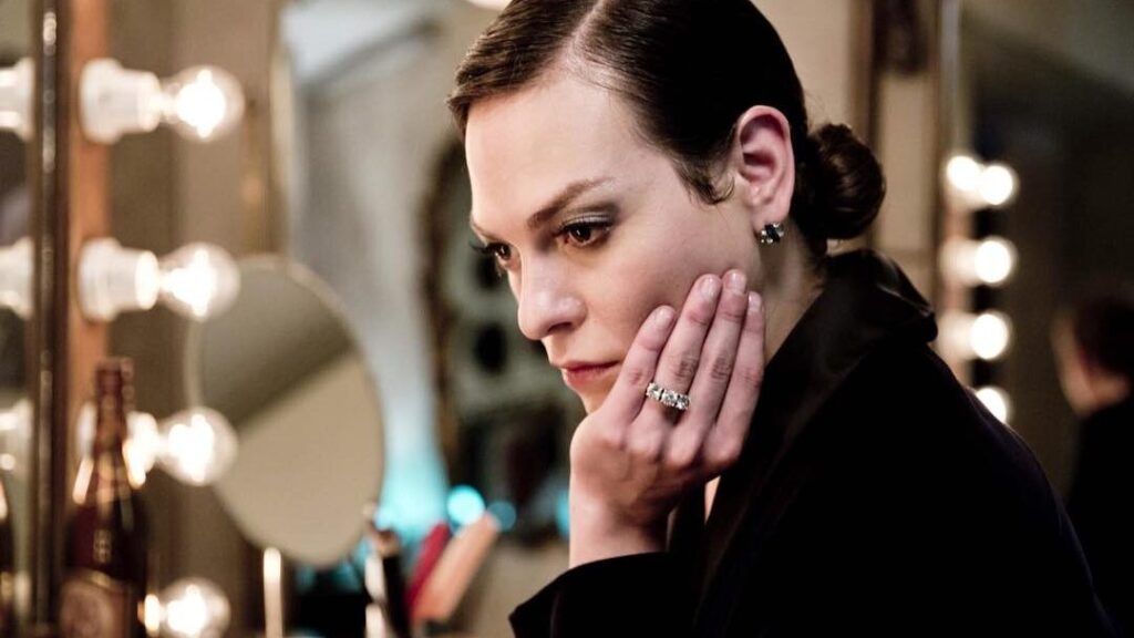Daniela Vega en el papel de Marina, con la cabeza apoyada sobre la mano, frente al espejo de un camarín, con una cálida iluminación ambiental.