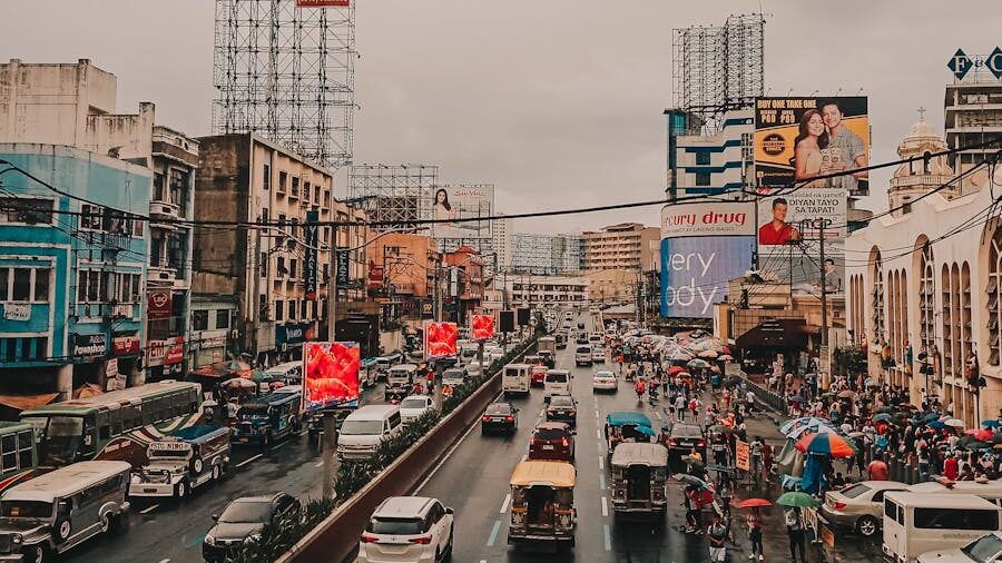 Calle urbana en Manila con tráfico, vendedores ambulantes con paraguas, carteles publicitarios y edificios comerciales bajo un cielo nublado.